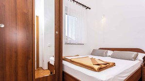 Quarto com cama de madeira, roupa de cama branca, janela com cortinas leves e guarda-roupa de madeira.