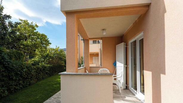 En balkon med et lille bord og stole, en glasdør og udsigt til en nabobygning.