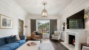 A living room with a blue sofa, a coffee table, a fireplace, and a television mounted above it. - EXPO Oasis-Heart of Tulsa! (Tulsa)