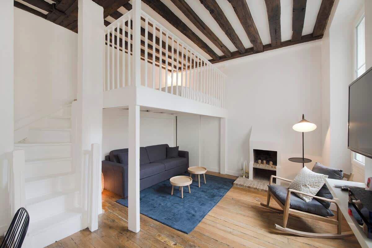 Un soggiorno in stile loft con soffitto alto, una scala, un divano, un tavolino, una poltrona a dondolo e un camino.