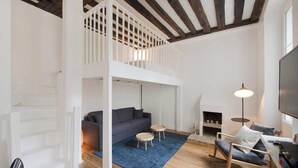 Ein Loft-Wohnzimmer mit hoher Decke, einer Treppe, einem Sofa, einem Couchtisch, einem Schaukelstuhl und einem Kamin.