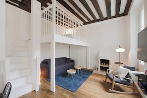 Uma sala de estar estilo loft com pé direito alto, uma escada, um sofá, uma mesa de centro, uma poltrona de balanço e uma lareira.