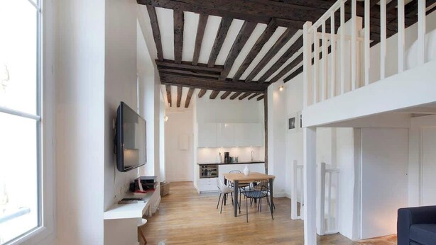 Ein modernes Interieur mit Holzboden, einem Essbereich mit Tisch und Stühlen, einem an der Wand befestigten Fernseher und einer Treppe, die zu einer oberen Ebene führt.