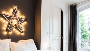 A hotel room with a star-shaped light fixture on the wall, a bed with white linens, and a view of the outdoors through a window with curtains.