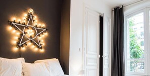 A hotel room with a star-shaped light fixture on the wall, a bed with white linens, and a view of the outdoors through a window with curtains.