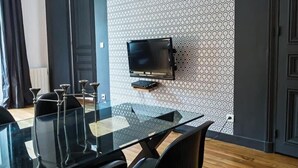 A modern dining area with a glass table, black chairs, and a mounted television.
