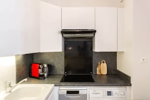 Uma cozinha compacta com um fogão por indução preto, uma máquina de lavar louça Bosch e uma cafeteira vermelha.
