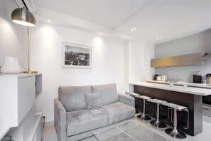 A modern living room with a grey sofa, a coffee table, and a bar area with stools.