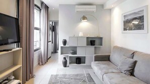 A modern living room with a grey sofa, a flat-screen TV, a white console table, and a large window with curtains.