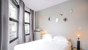 A hotel room with a large bed, a nightstand with a lamp, and a wall-mounted mirror.