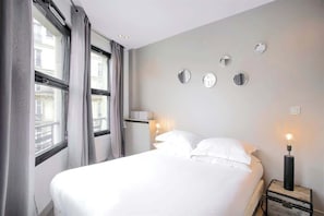 Quarto de hotel com uma cama grande, mesa de cabeceira com abajur e espelho fixado na parede.