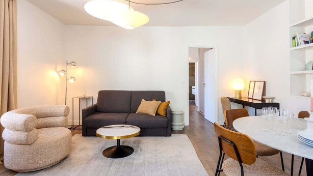 A modern living room with a sofa, round coffee table, and dining table set for four.