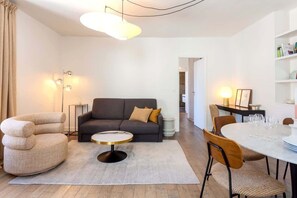 Uma sala de estar moderna com sofá, mesa de centro redonda e mesa de jantar posta para quatro pessoas.