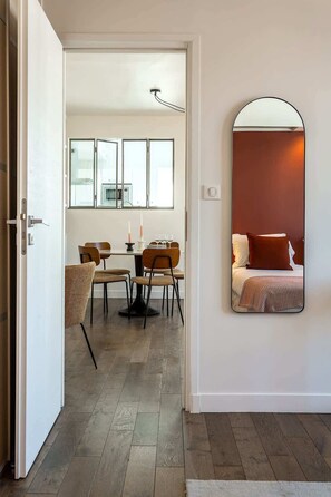 A hotel room with a dining area, a large mirror, and a bed with a red pillow.