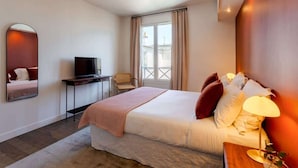 A hotel room with a bed, a television, a desk, a chair, and a window with curtains.