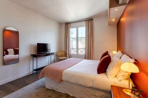 Une chambre d’hôtel équipée d’un lit, d’une télévision, d’un bureau, d’une chaise et d’une fenêtre avec des rideaux.
