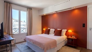 A bedroom with a large bed, two bedside lamps, a desk with a chair, and a window with curtains.