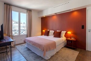 Une chambre à coucher avec un grand lit, deux lampes de chevet, un bureau avec une chaise et une fenêtre avec des rideaux.