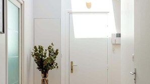 A hallway with a white door, a small table with a plant, and a skylight above.