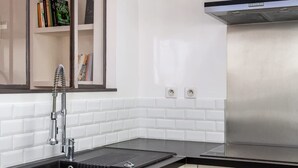 A modern kitchen with white cabinetry, a black countertop, stainless steel appliances, and a built-in bookshelf.