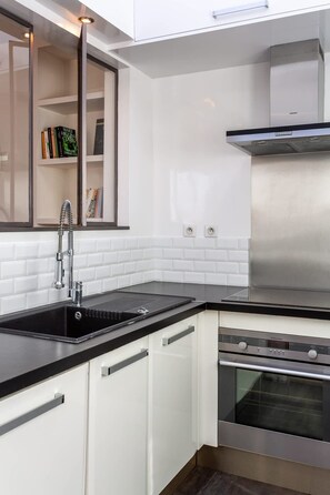Une cuisine moderne avec des meubles blancs, un plan de travail noir, des appareils électroménagers en acier inoxydable et une bibliothèque intégrée.