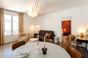 Uma sala de estar moderna com uma mesa de jantar redonda posta para quatro pessoas, um sofá e uma pequena mesa lateral com abajur.