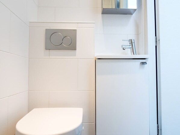 A bathroom with a white toilet, a wall-mounted bidet, and a small sink with a faucet.