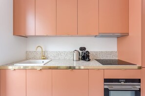 Een keuken met perzikkleurige kastjes, een wit aanrecht, een gouden kraan, een waterkoker en een koffiezetapparaat.