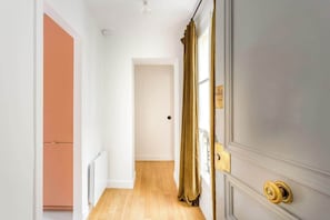 Un couloir avec un plancher en bois, une porte fermée dotée d’une poignée dorée et un radiateur fixé au mur.