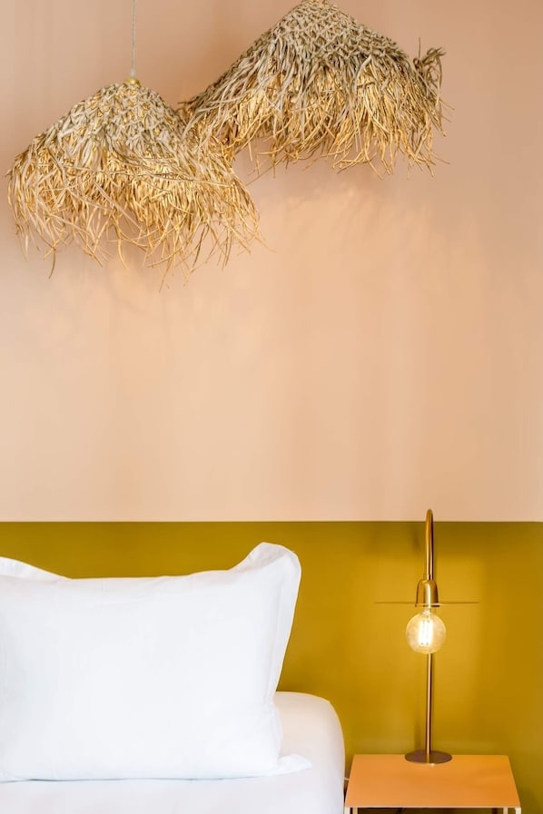 Un lit avec une literie blanche, une lampe de chevet et un luminaire suspendu fait de matériaux naturels.