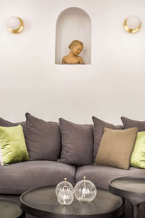 Un salon moderne avec un canapé gris, des coussins verts et beiges, et deux vases en verre transparent posés sur une table basse ronde.