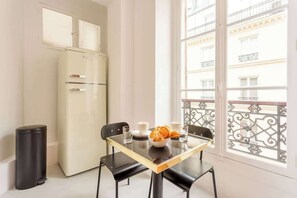 Een kleine, moderne kamer met een witte koelkast, een tafel met een schaal croissants, twee bekers en een glas.