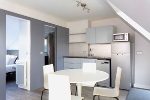 Um espaço compacto com cozinha compacta, área de refeições com mesa redonda e cadeiras, e um espaço de dormir separado com uma cama.