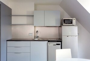 Uma cozinha compacta com micro-ondas, frigorífico, máquina de lavar loiça e lava-loiça.