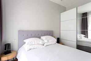 A modern bedroom with a large bed, a nightstand, a lamp, and a mirror.