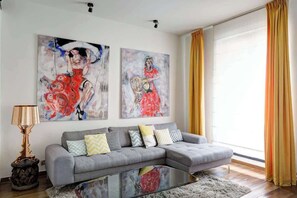 A modern living room with a grey sectional sofa, a glass coffee table, and two abstract paintings on the wall.