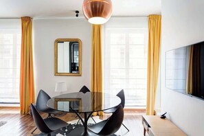 A modern living room with a round glass table, black chairs, a large mirror, and a flat-screen TV.