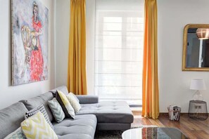 A modern living room with a grey sectional sofa, a glass coffee table, and a large window with yellow curtains.