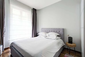 Quarto moderno com cama grande, cabeceira e mesa de cabeceira com abajur.
