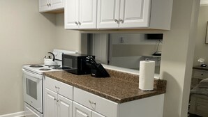 A kitchen with white cabinets, a stove, microwave, and a trash can. - Adventure Acres- Suite C8  (Holly)
