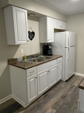 A compact kitchen with white cabinetry, a granite countertop, a built-in refrigerator, and a coffee maker. - Adventure Acres- Suite C8 (Holly)