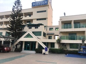 A hotel with a prominent sign, a staircase, and a statue in the foreground. - Korkdam Hotel (Accra)