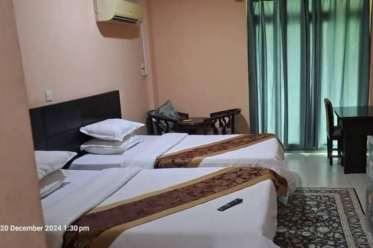 A hotel room with two beds, a desk, a chair, a small refrigerator, and a window with curtains.