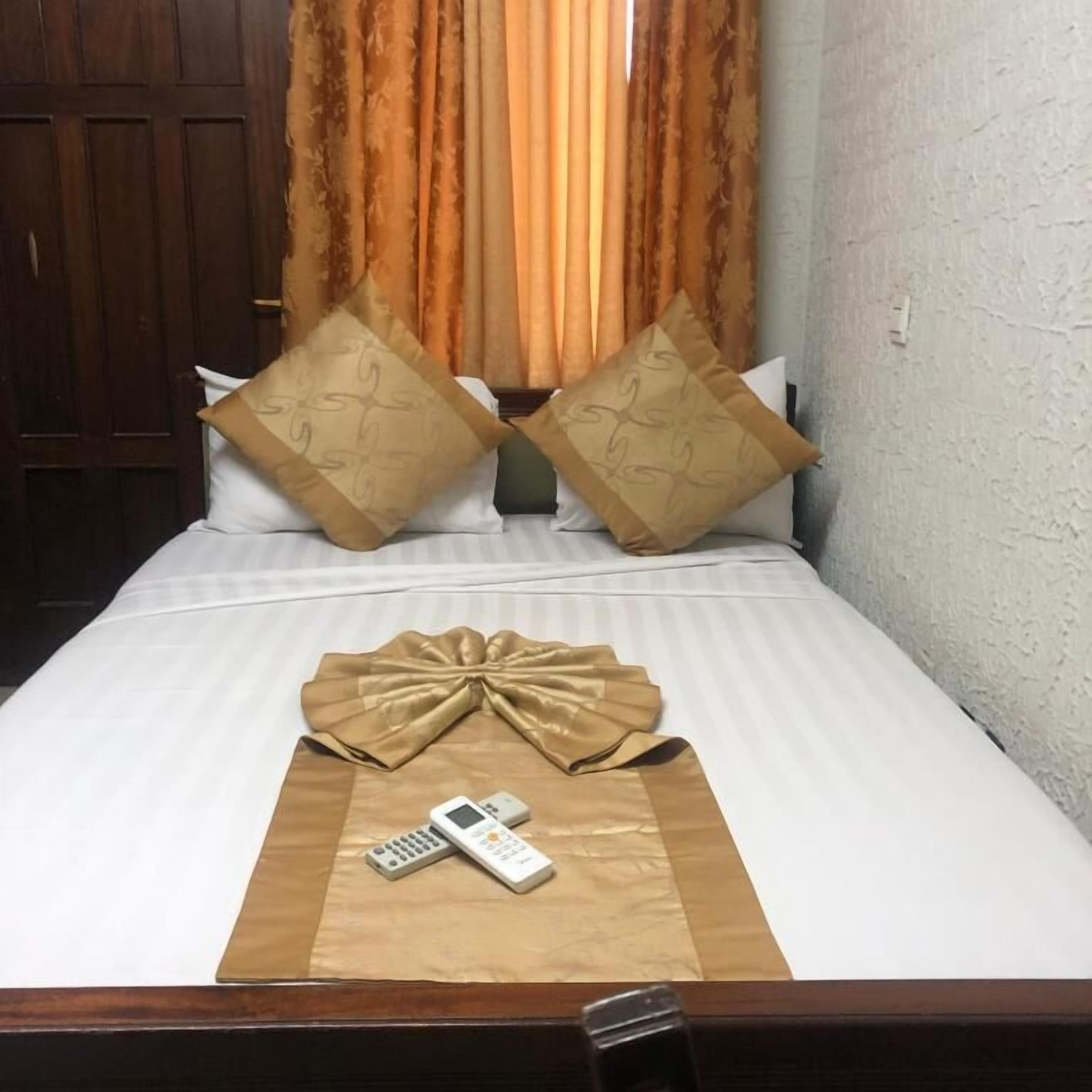 Un lit bien fait, agrémenté d’un coussin décoratif, d’une télécommande et d’un téléphone intelligent posés sur une couvre-lit.