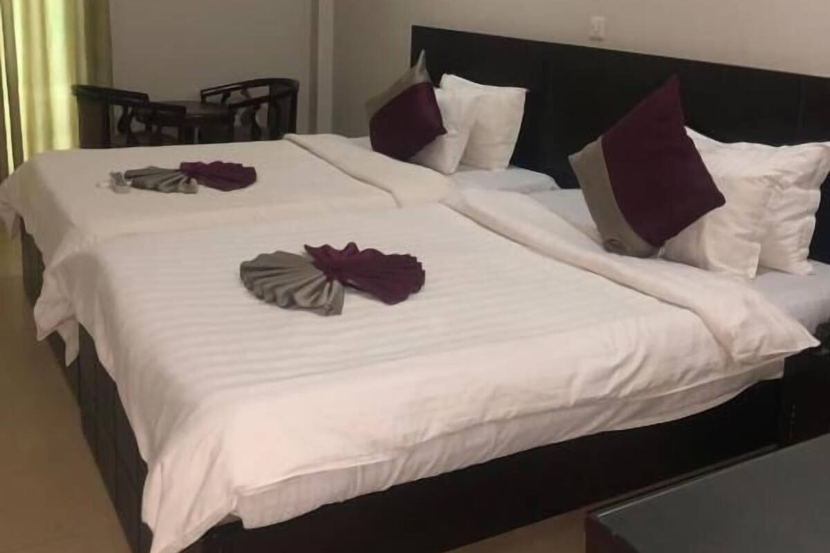A hotel room with two beds, a desk, and an air conditioning unit.