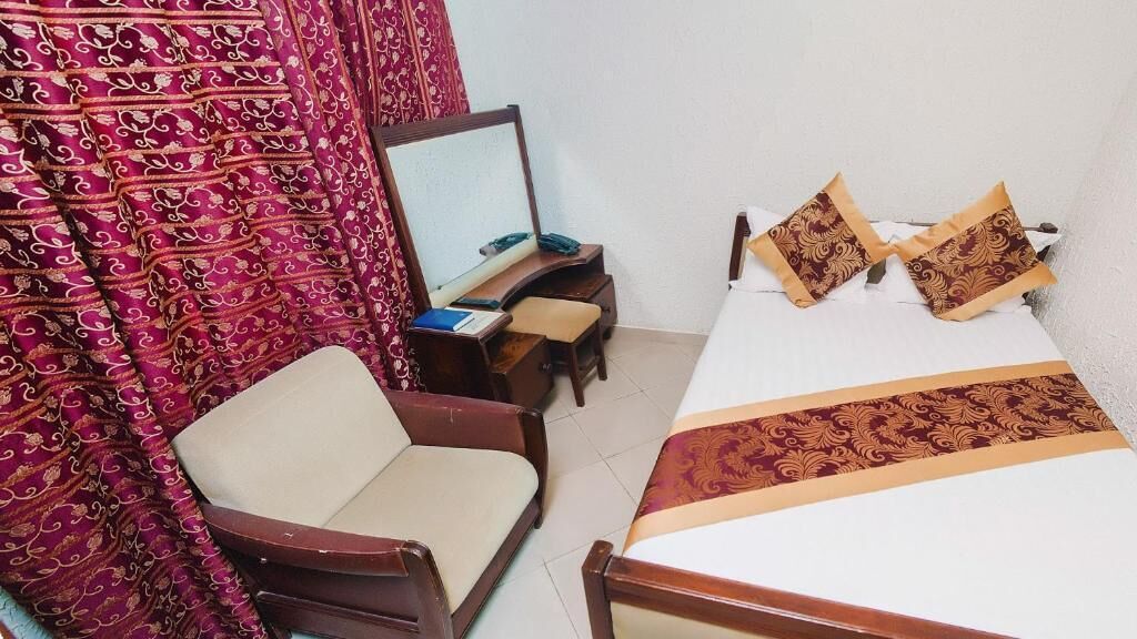 A bedroom with a bed, a chair, a desk with a mirror, and a patterned curtain.