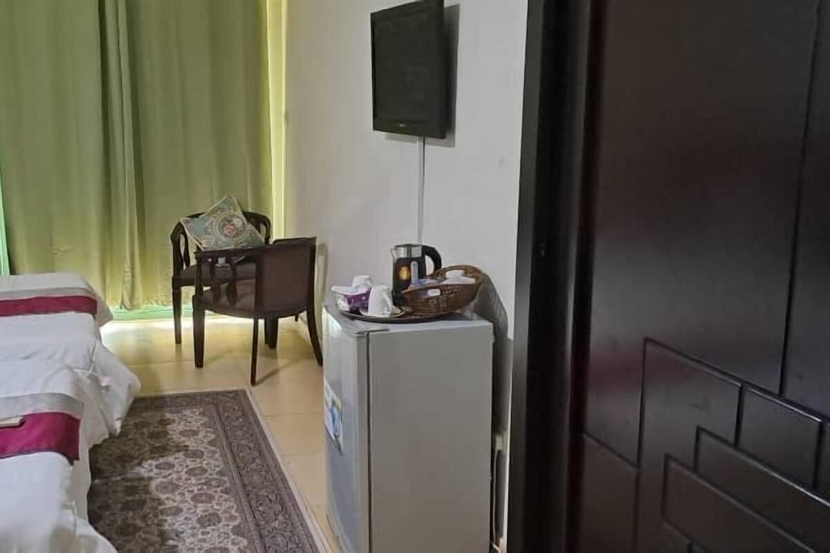 A hotel room with a bed, a desk, a chair, a television, and a refrigerator.