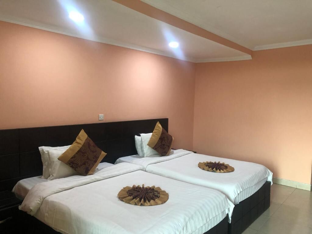 Quarto de hotel com duas camas, paredes cor de pêssego e cabeceira escura.