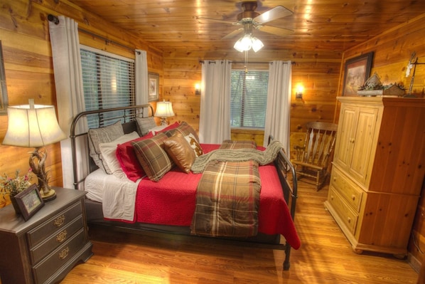 A wooden cabin bedroom with a bed, nightstands, a dresser, and a ceiling fan.