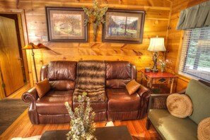 A cozy living room with a leather sofa, a small side table, a lamp, and two framed pictures on the wall.